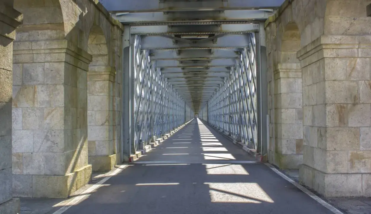 El **puente internacional Tui** se alza imponente, un túnel de metal y piedra que se pierde en la distancia, proyectando sombras geométricas sobre el asfalto.