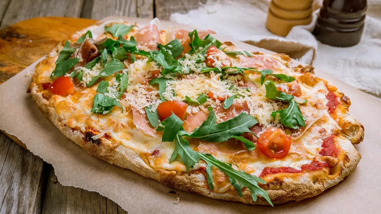 Eine leckere Pinsa belegen mit Schinken, Rucola und Kirschtomaten. Käse und Tomatensauce runden den Genuss ab.