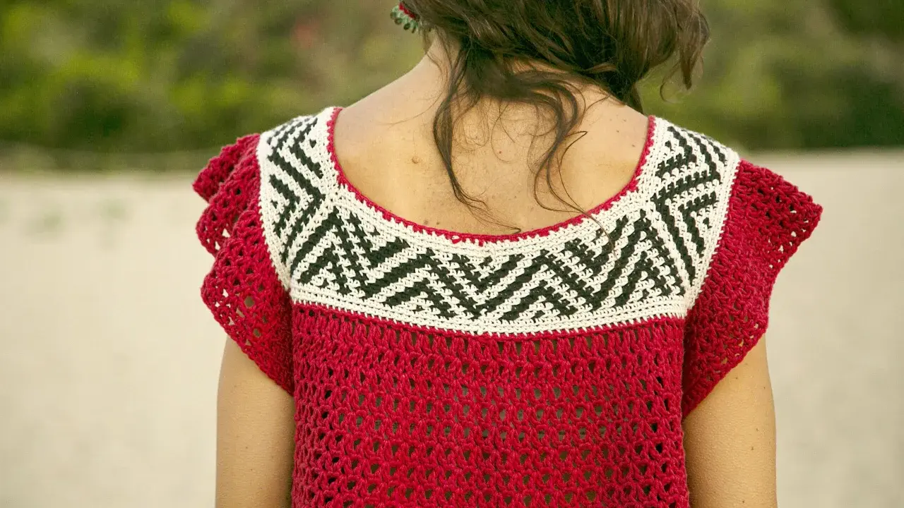 Detalle de un top de ganchillo rojo con un patrón geométrico blanco y negro en el cuello.
