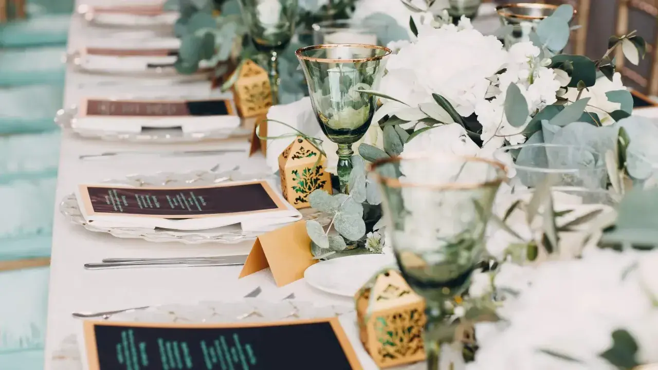 Eleganckie nakrycia stołu na wesele bez alkoholu: zielone kieliszki, menu, ozdobne pudełeczka i bukiety.