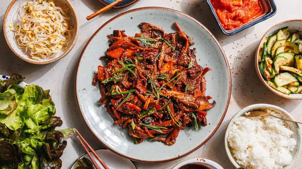 Ein köstliches koreanisches BBQ-Rezept mit gebratenem Fleisch, Beilagen wie Kimchi, Gurkensalat, Sprossen und Reis.