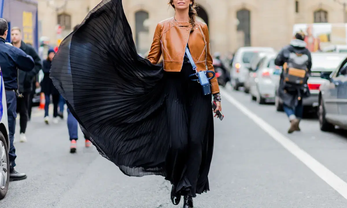 Donna con gonna nera plissettata e giacca in pelle marrone, un look audace che esprime la sua lybido abbigliamento.
