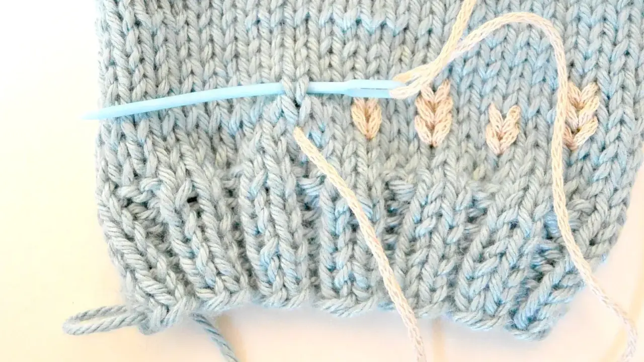 Agujas de punto plumeti dos agujas, creando un delicado diseño de hojas en tejido azul claro.