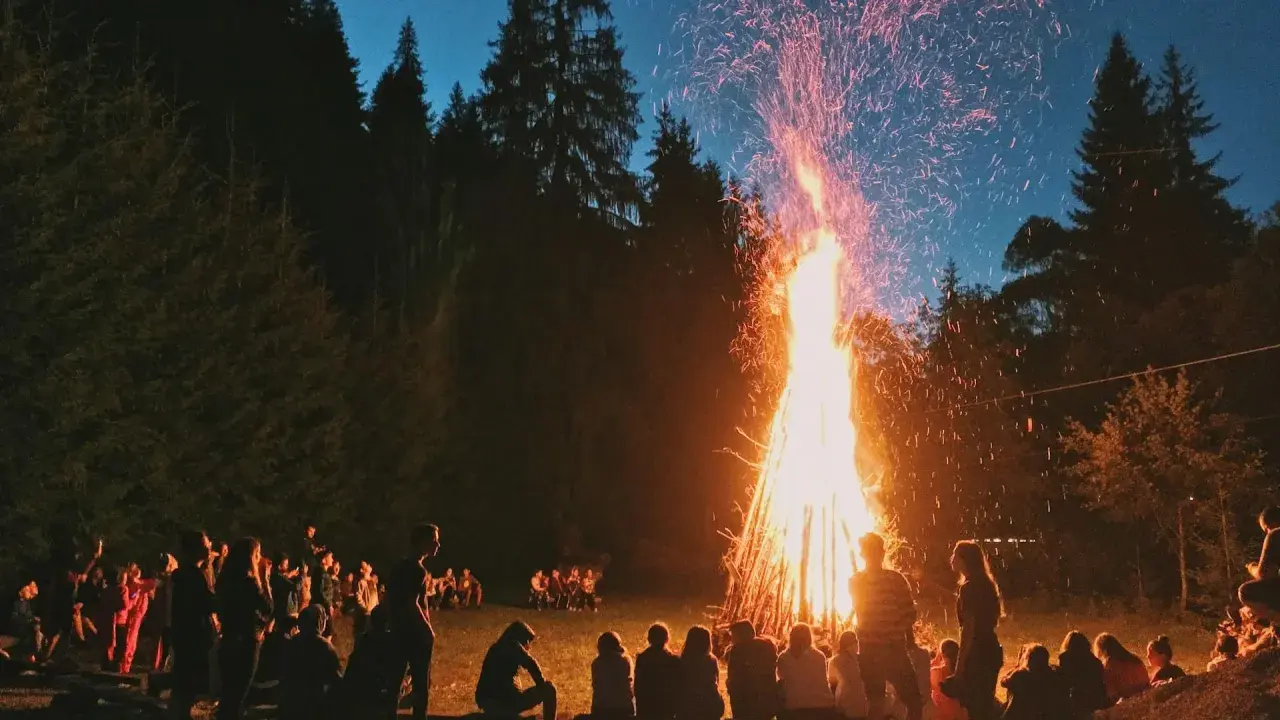 Människor samlas runt en stor brasa i skogen, en vacker svensk tradition som lyser upp natten med gnistor och värme.