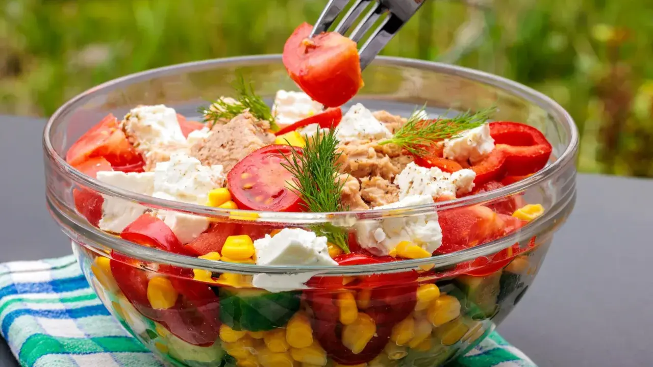 Szybkie i tanie sałatki to idealny pomysł na lekki posiłek. W szklanej misce kolorowa sałatka z pomidorów, ogórka, kukurydzy, papryki, sera feta i tuńczyka.