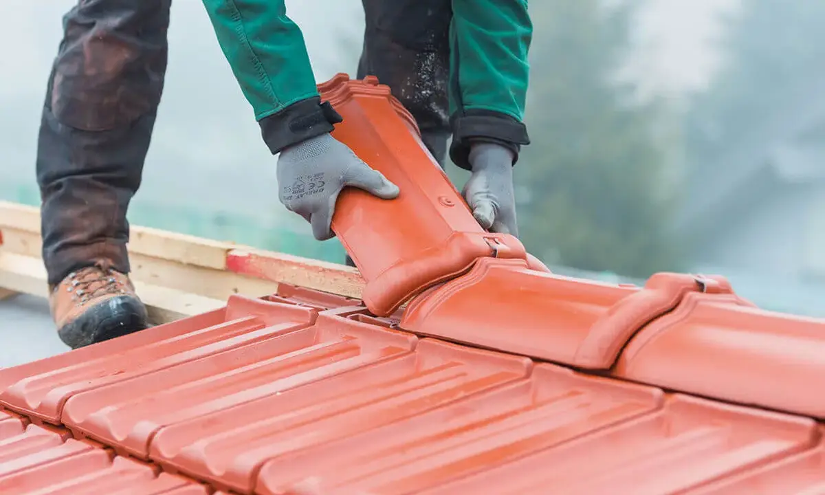 Dachówka ceramiczna w rękach dekarza. Czy remont dachu wymaga pozwolenia na budowę? Zależy od zakresu prac.