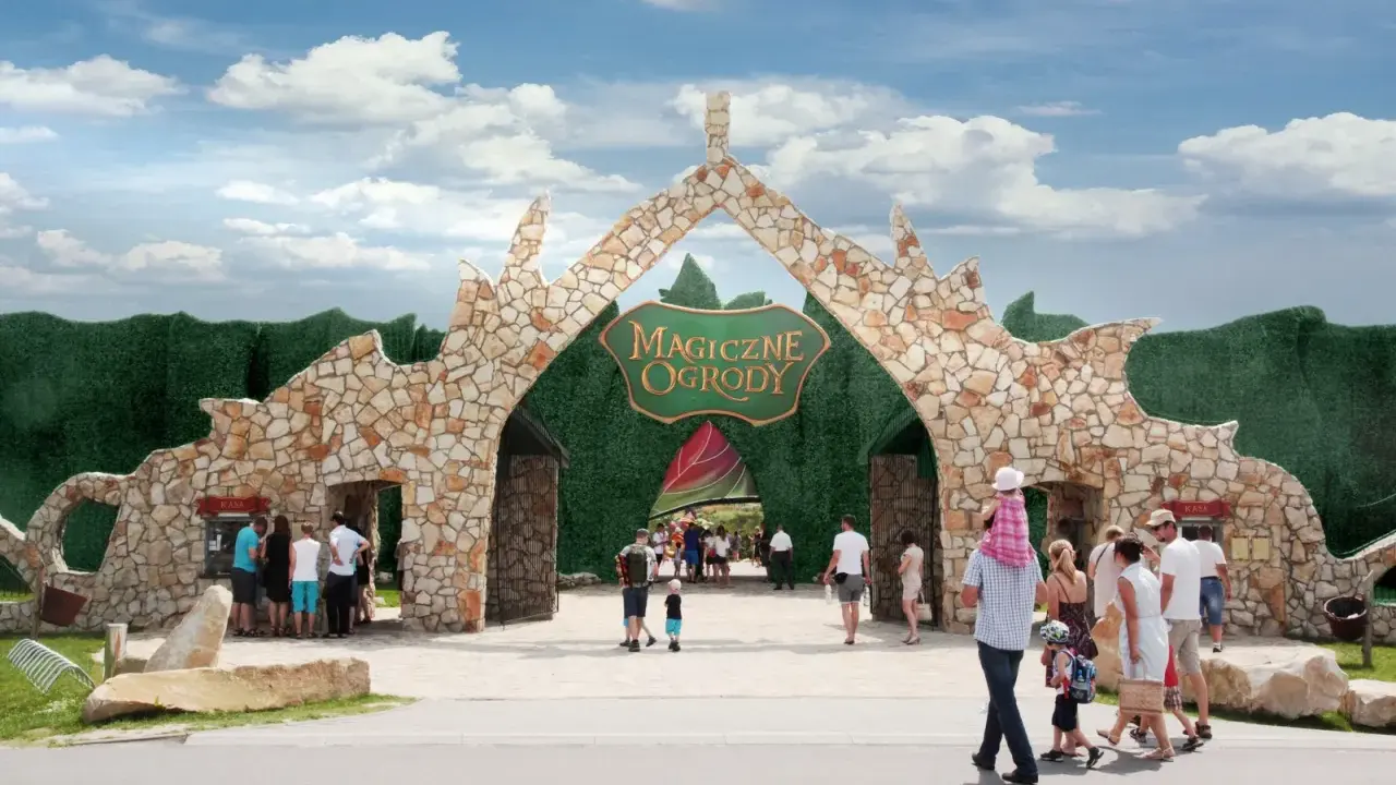 Kamienna brama z napisem "Magiczne Ogrody" zaprasza na niezapomniane atrakcje dla dzieci mazowieckie. Rodziny wchodzą do bajkowego świata.