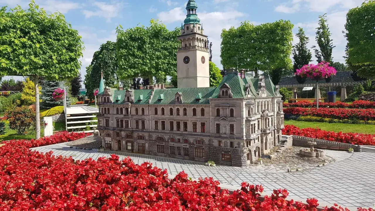 Miniatura ratusza z wieżą zegarową, otoczona czerwonymi kwiatami. Jedna z wielu atrakcji Kotliny Kłodzkiej.