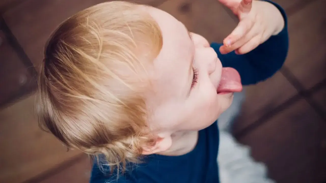 Małe dziecko nie słucha w przedszkolu, wyciąga język i bawi się jedzeniem.
