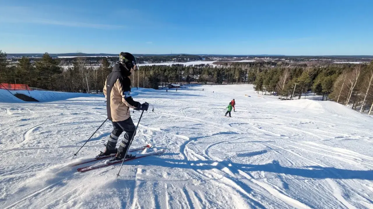 Person åker skidor i Luleå en solig dag. Barn åker skidor i bakgrunden.
