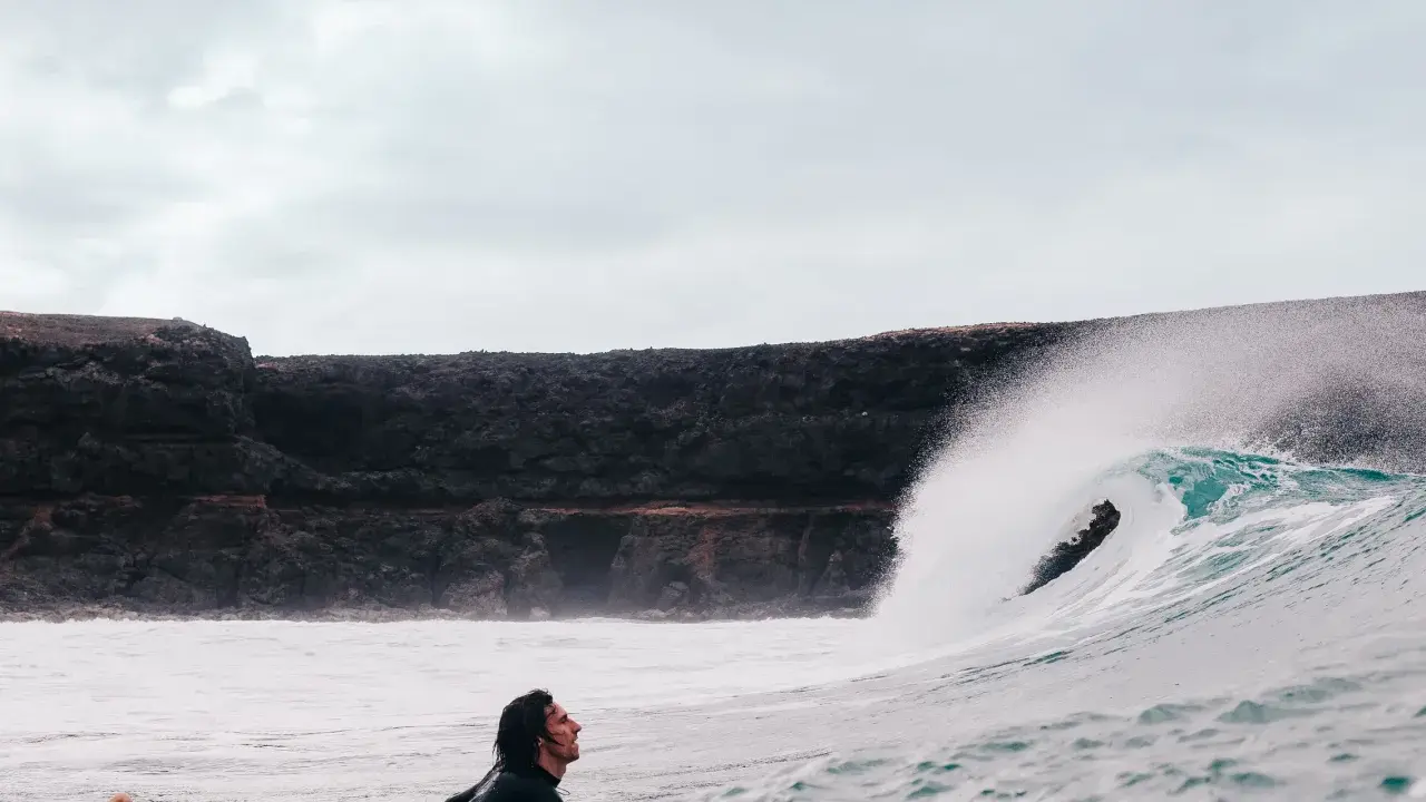 Surfer wartet auf die perfekte Welle vor der Felsküste. Windsurfen Fuerteventura.