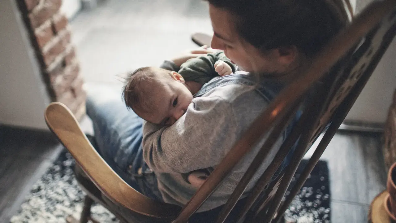 Ein Baby schläft friedlich auf dem Arm einer Person, die in einem Schaukelstuhl sitzt. Es ist, als ob die Babys im Bauch noch träumen, bevor sie die Welt entdecken.