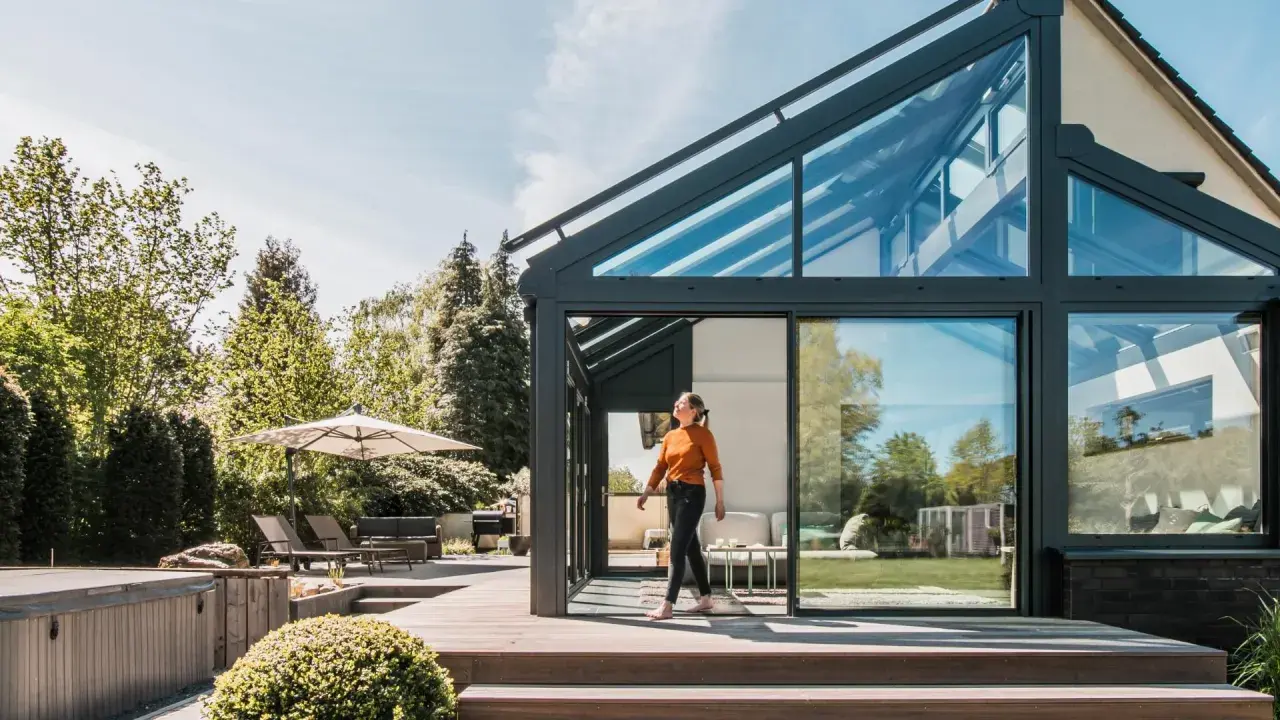 Frau betritt modernen Wintergarten mit Glasdach. Perfekt, um den Sommer zu verlängern und den **Wintergarten planen**.