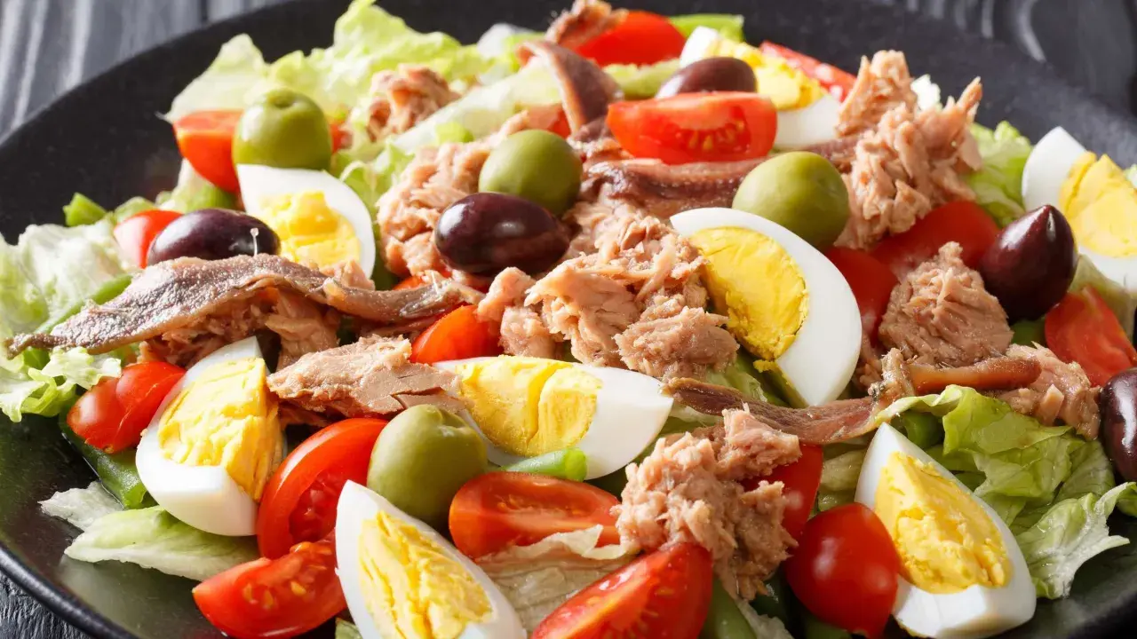 Ein bunter Nizza Salat mit Thunfisch, Ei, Tomaten, Oliven und Sardellen auf knackigem Salatbett.