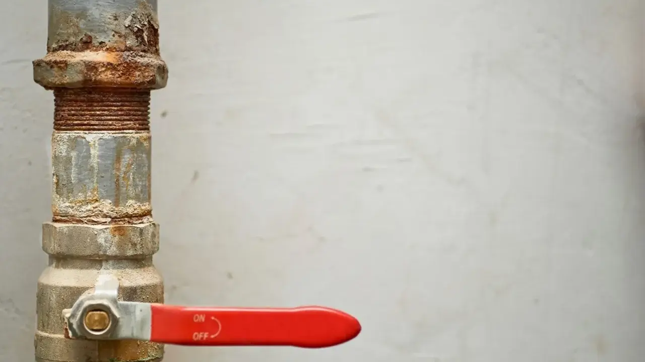 Tubería oxidada con una llave de paso general roja, lista para controlar el flujo.