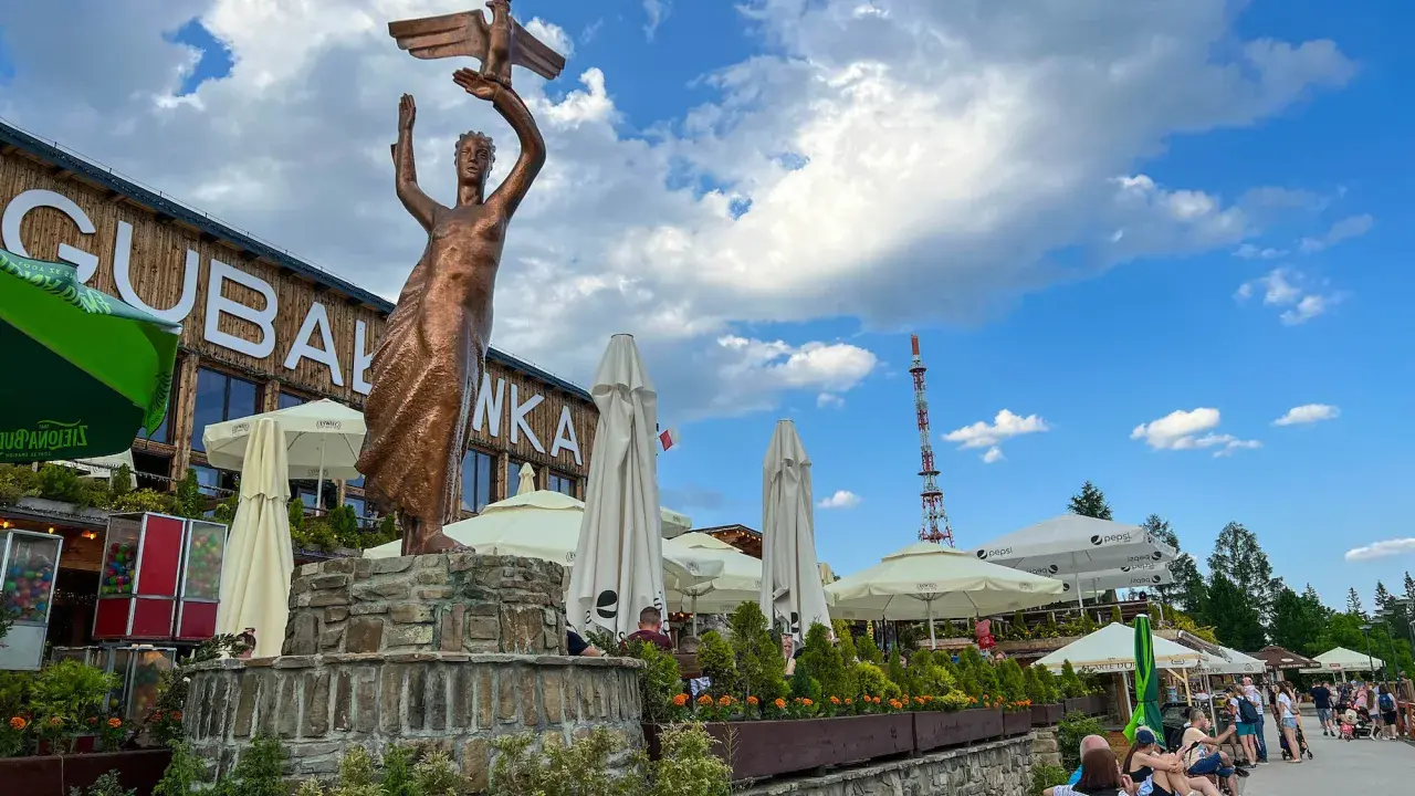 Gubałówka atrakcje: pomnik z orłem, restauracje, parasole i ludzie odpoczywający na ławkach.