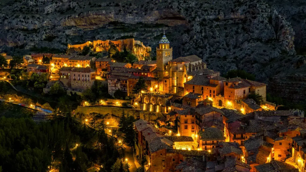 Pueblo iluminado al anochecer, ideal para planes para el puente de diciembre. Casas de piedra y tejados se asoman entre la montaña.