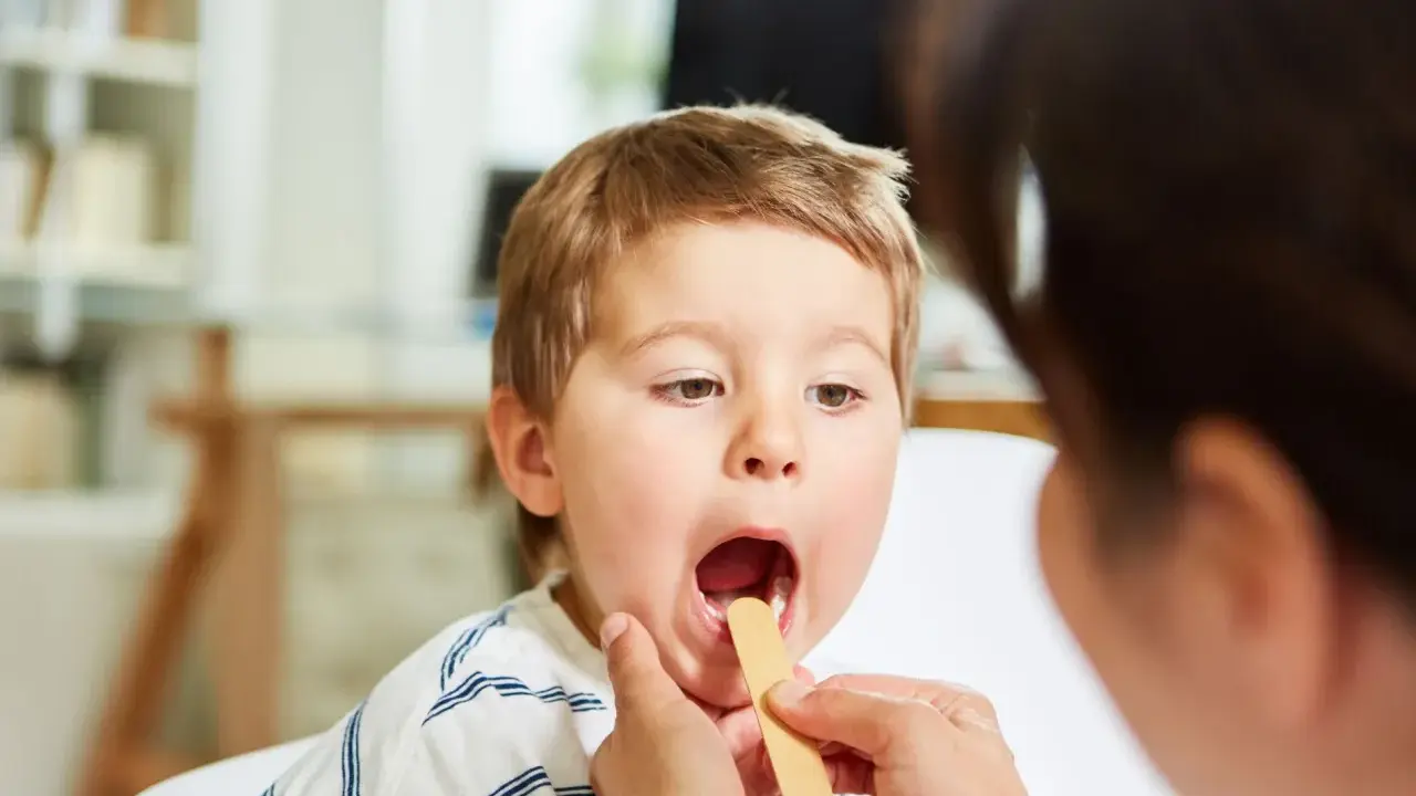 Bambino con bocca aperta durante visita medica per sospetta laringite.
