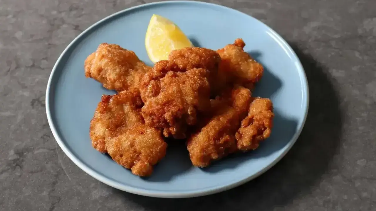 Chrupiący kurczak karaage na niebieskim talerzu, z kawałkiem cytryny.