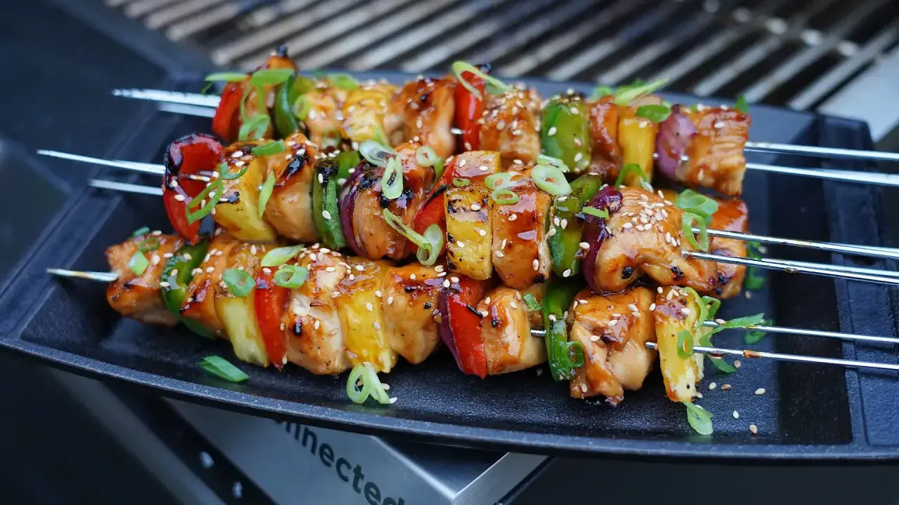 Huli Huli Chicken Spieße mit Paprika, Zwiebeln und Ananas, glasiert und mit Sesam bestreut, auf einem Grill.