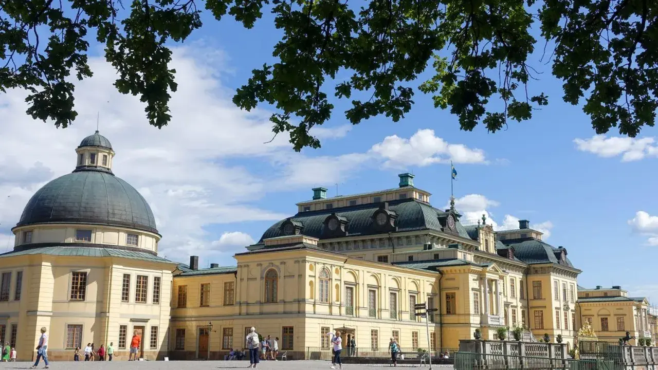 Drottningholms slott, där kungen bor, med sin imponerande kupol och gula fasader under en blå himmel med moln.