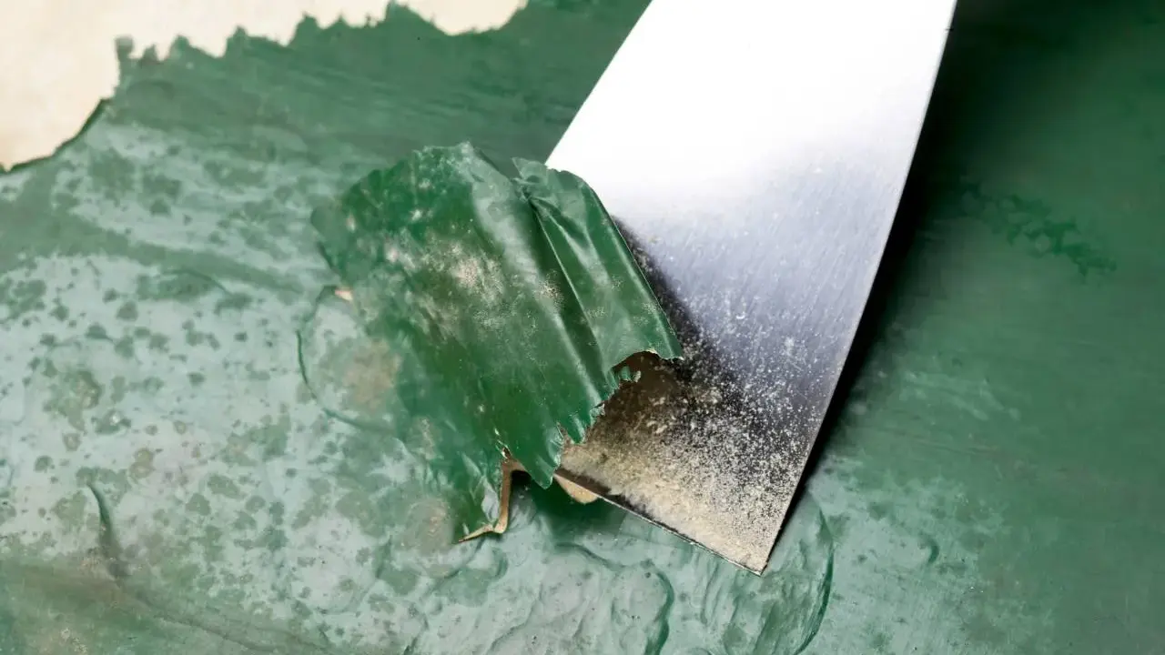 Espátula metálica retirando pintura verde descascarada de una pared. Proceso de cómo quitar pintura de la pared.