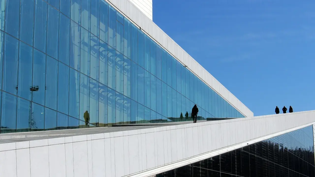 Nowoczesna architektura Uniwersytetu w Oslo z lustrzaną fasadą odbijającą niebo i ludzi.