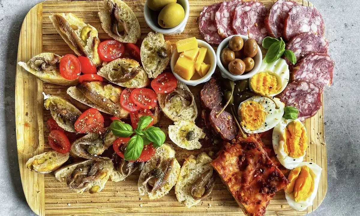 Ein köstlicher Antipasti-Abend mit Bruschetta, Sardellen, Tomaten, Oliven, Käse, Eiern und Salami auf einem Holzbrett.