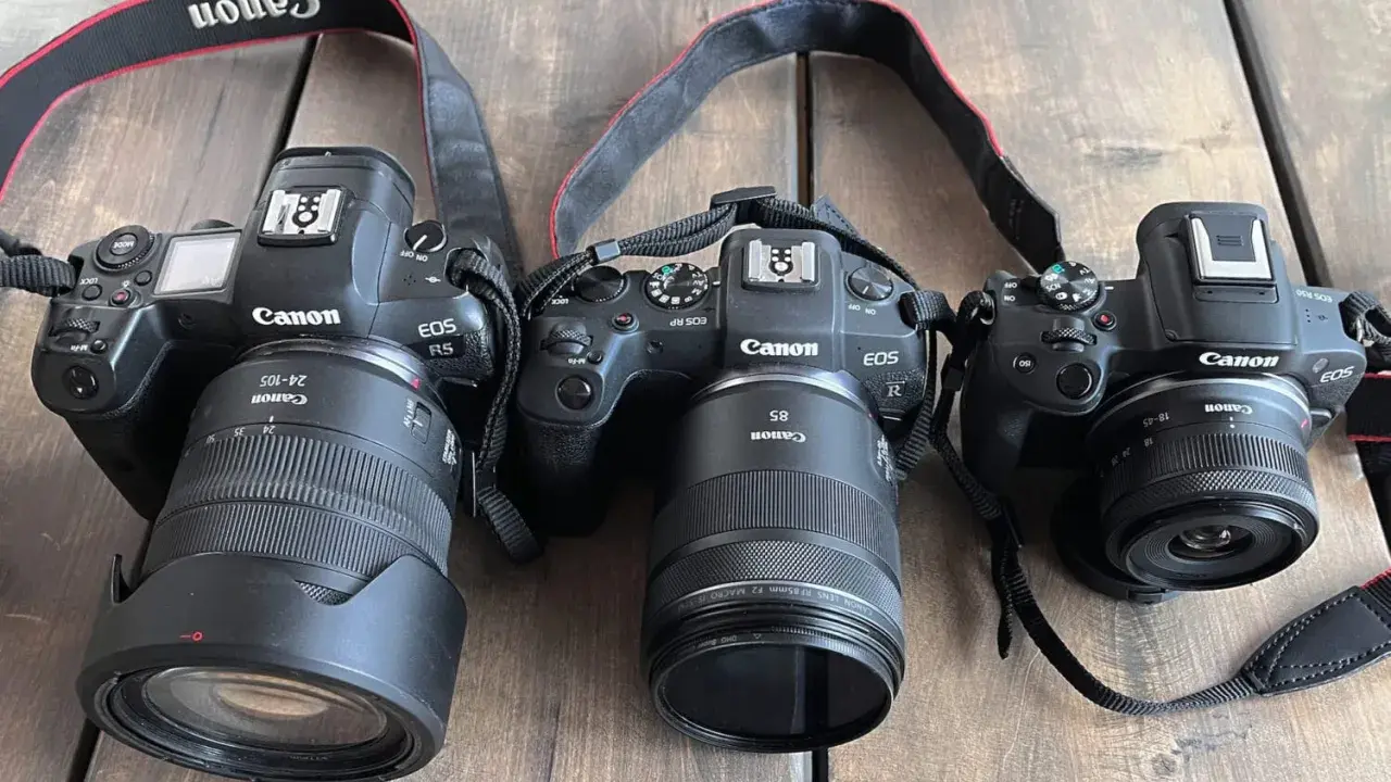 Trzy aparaty Canon EOS R, RP i R5 z obiektywami leżą obok siebie. Pełna klatka w całej okazałości.