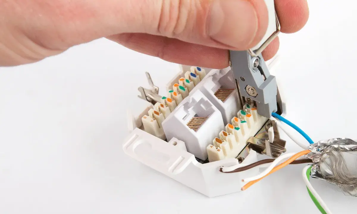 Hand legt Kabel an Netzwerkdose auf. Werkzeug drückt blaue Ader in LSA-Leiste.