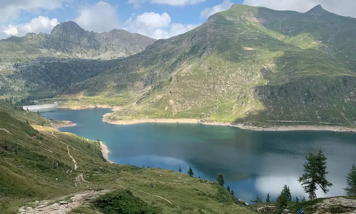 Sentiero facile tra i laghi gemelli alpini, con montagne verdi e un cielo azzurro con nuvole bianche.