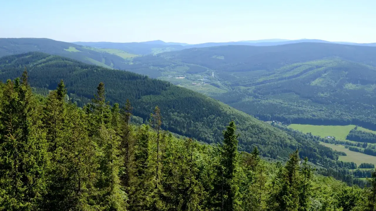 Zielone, zalesione zbocza Gór Opawskich schodzą ku dolinie z polami i zabudowaniami.