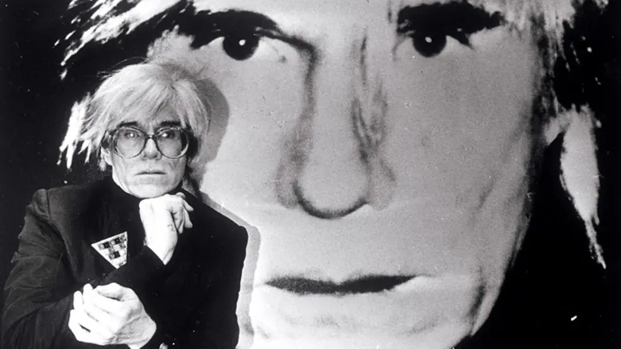 Andy Warhol, Ikone der Pop Art, posiert vor einem riesigen Porträt von sich selbst. Seine Kunstrichtung prägte die moderne Kunst.