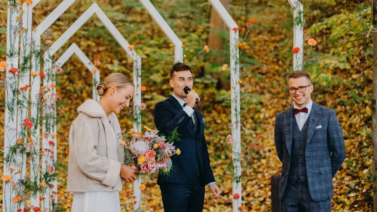 Piękna panna młoda z bukietem, pan młody przemawia do mikrofonu, a pan młody z uśmiechem. Wesele jesienią w otoczeniu kolorowych liści.