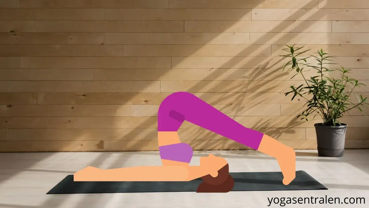 En person utför plogen yoga på en matta framför en trävägg.