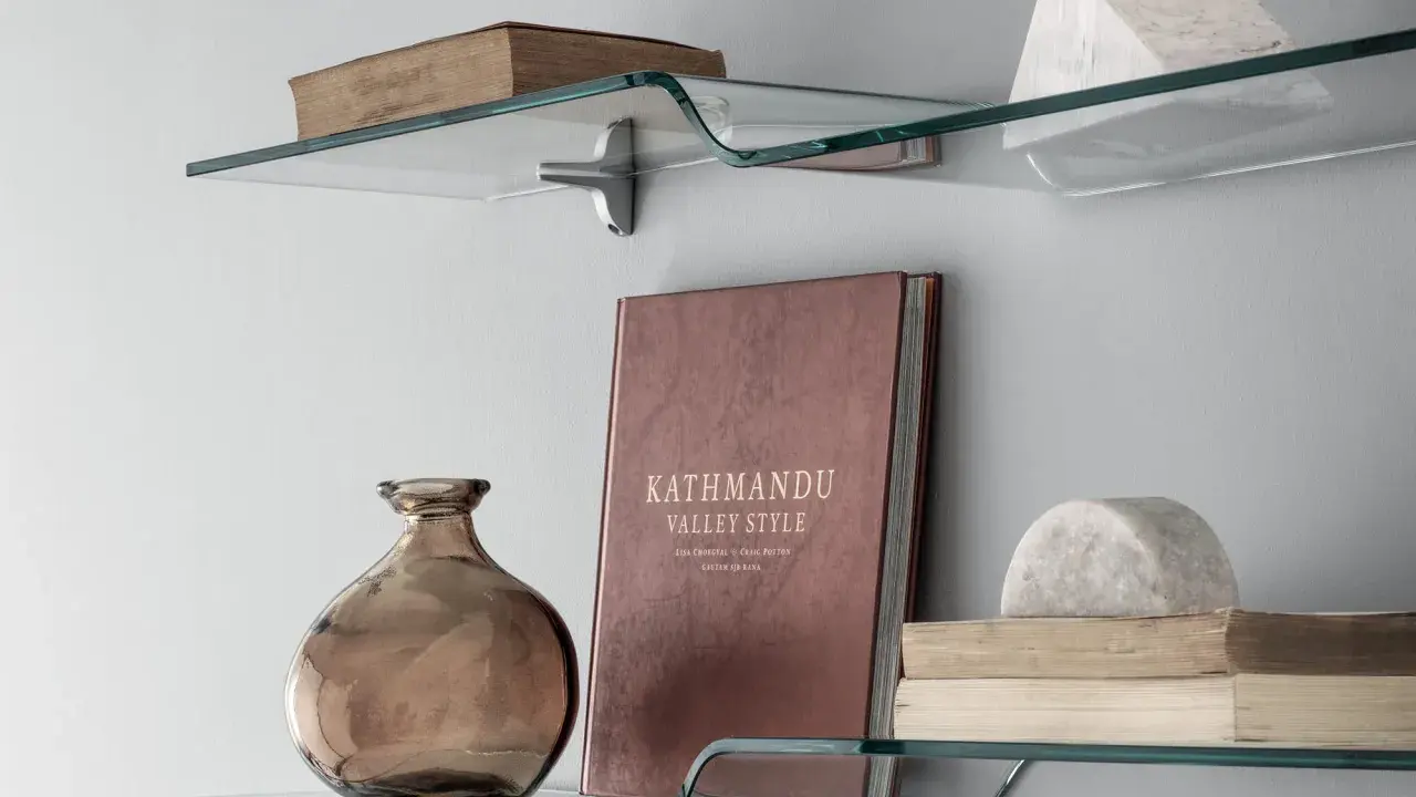 Idee mensole ingresso: vetro curvo con libri antichi, vaso ambrato e scultura in marmo.