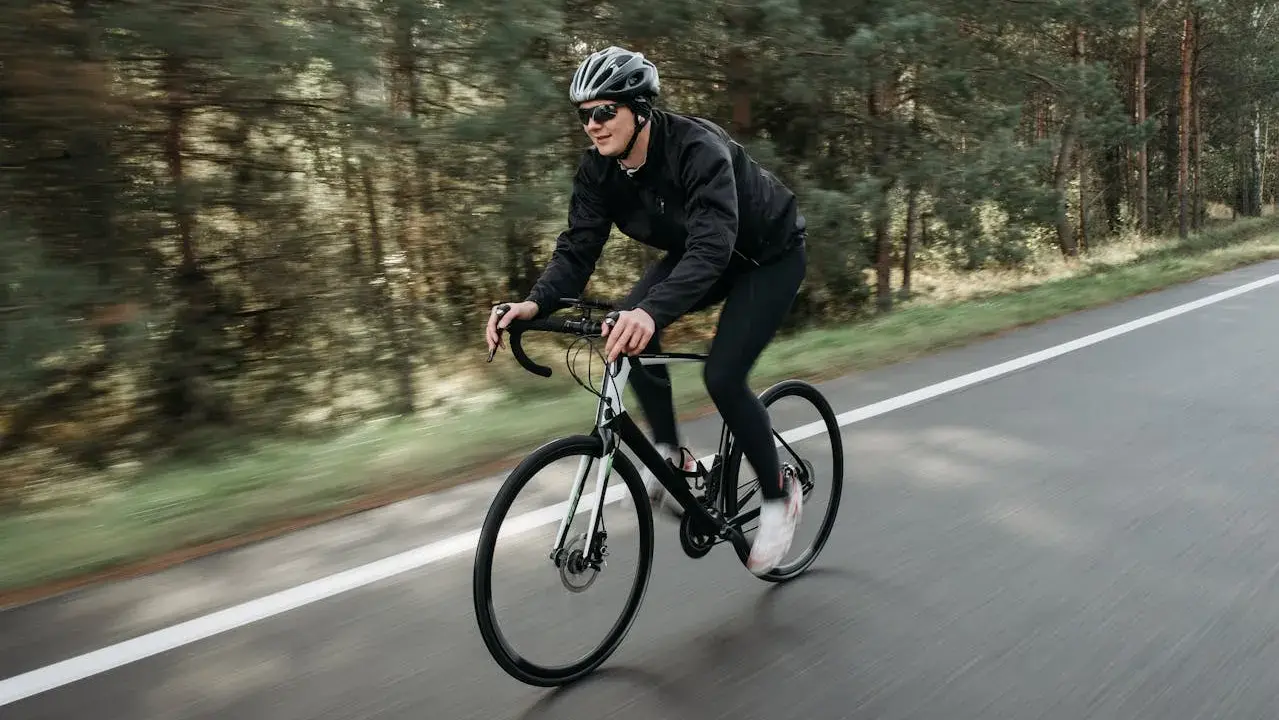 Mężczyzna w kasku i okularach jedzie na rowerze szosowym przez las. To świetny sposób, jak schudnąć na rowerze, poprawiając kondycję.