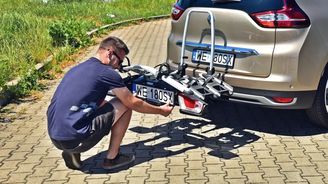 Mężczyzna montuje trzecią tablicę rejestracyjną WE 180SX na bagażniku rowerowym przy samochodzie.