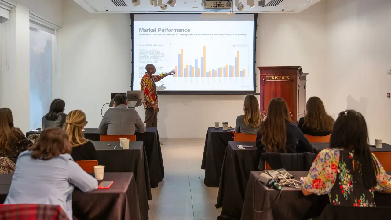 A presenter discusses market performance at Christie's, showing auction data to an audience.