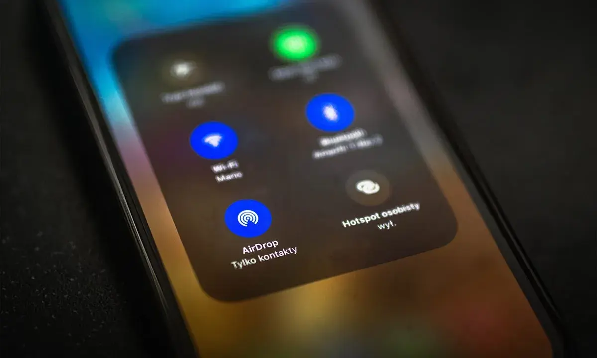 Ekran telefonu z widocznym menu, gdzie opcja AirDrop jest podświetlona. To funkcja do bezprzewodowego udostępniania plików między urządzeniami Apple.