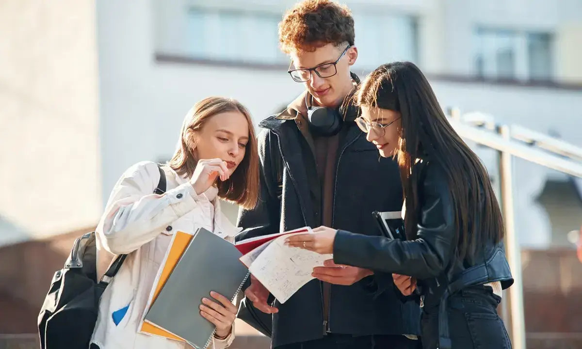 Trzech studentów dyskutuje nad notatkami, ich status ucznia widoczny w skupieniu i materiałach.