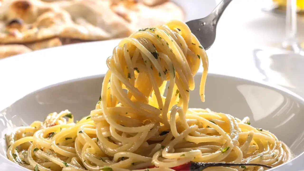 Pyszne dania z makaronem: spaghetti z ziołami i czosnkiem, na talerzu, z widocznym w tle pieczywem.