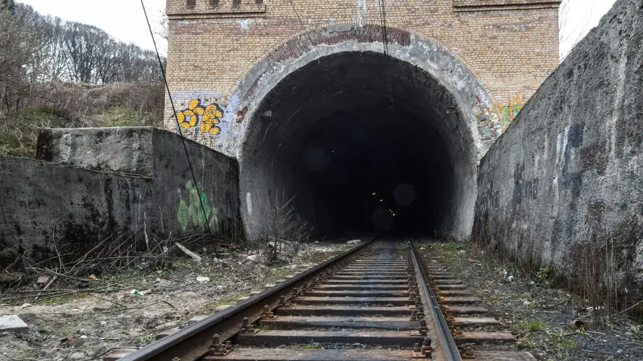 Torowisko prowadzi do ciemnego tunelu pod ceglanym łukiem z blankami, przypominającym bramę do dawnej kopalni Rydułtowy.