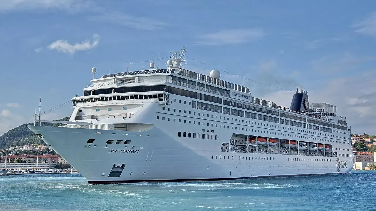 La MSC Armonia, con la sua impressionante lunghezza, solca le acque azzurre vicino a una costa collinare.