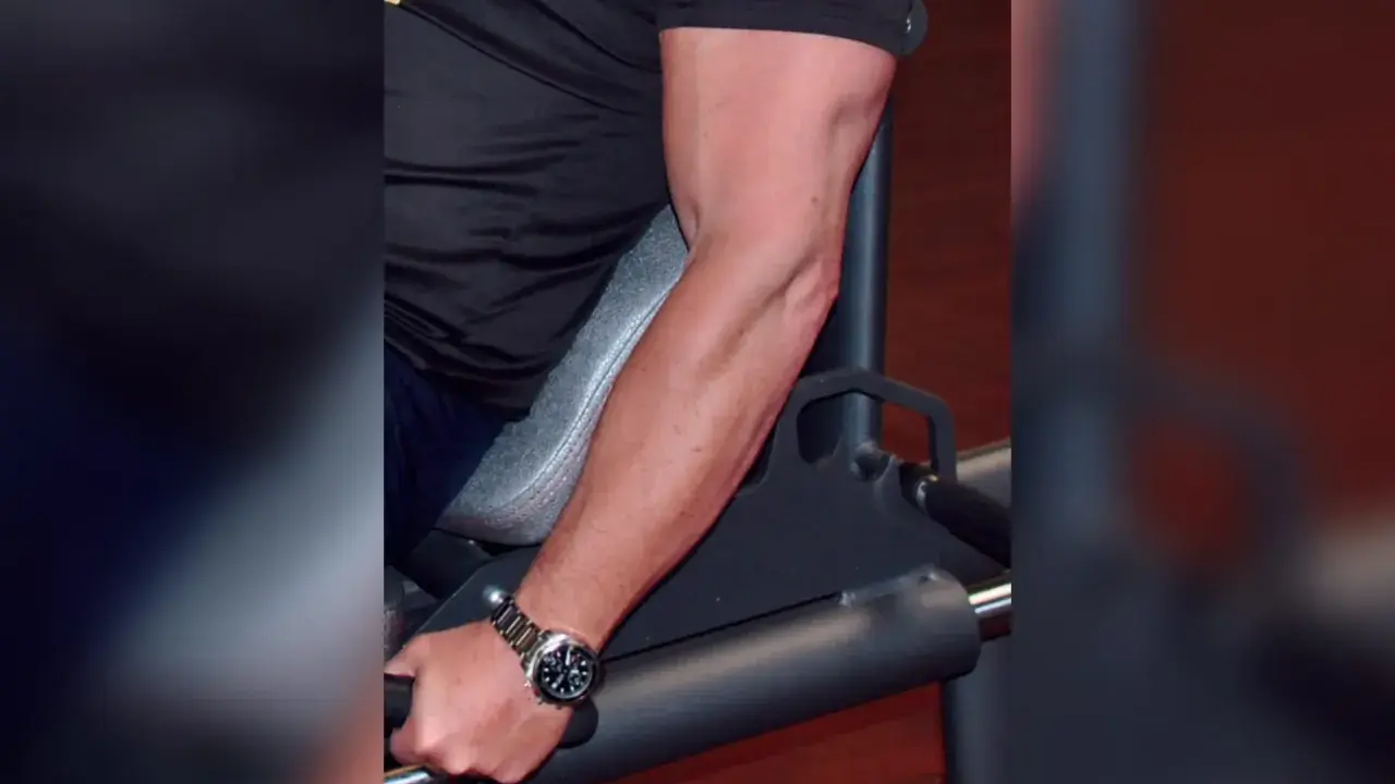 Mann trainiert unterarme im gym. Sein Bizeps ist gut sichtbar, während er sich auf ein Gerät stützt.