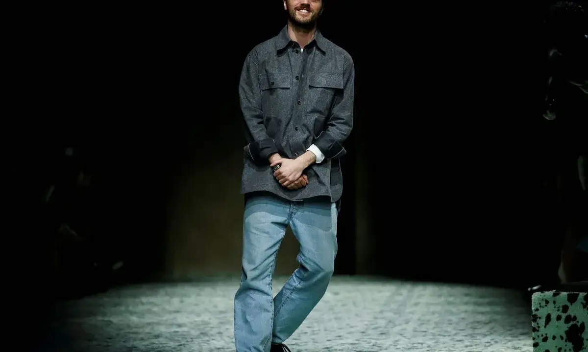 Matthieu Blazy, diseñador de Bottega Veneta, sonríe en la pasarela con camisa gris y vaqueros.