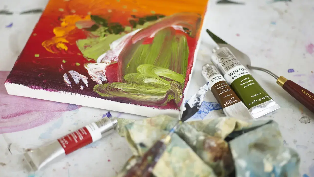 Płótno z barwnym obrazem, tubki farb olejnych Winsor & Newton, paleta i pędzle – idealne narzędzia, by dowiedzieć się, jakimi farbami malować na płótnie.