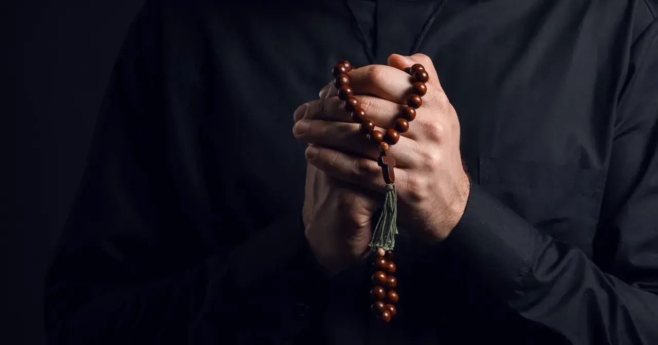 Dłonie księdza trzymające paciorki różańca, symbol wiary i nadziei w obliczu trudów życia, gdzie pańszczyzna a kościół splatały się w historii.