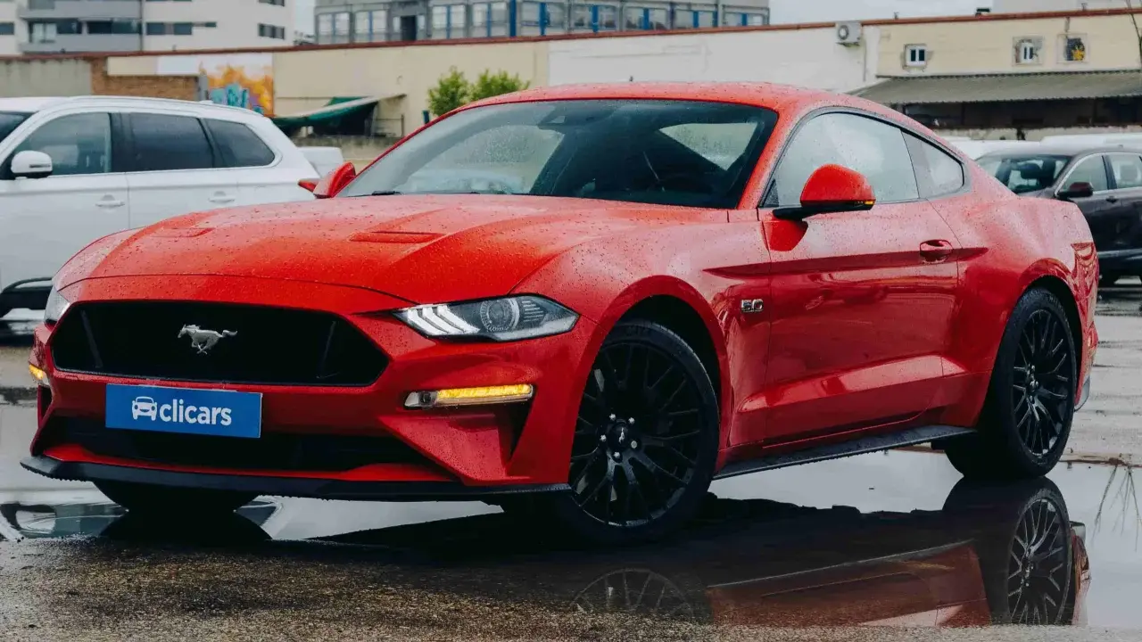 Un deportivo rojo, que es un coche coupe, brilla bajo la lluvia.