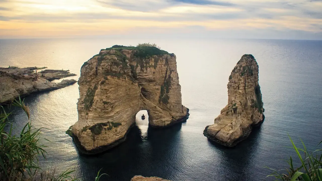 Felsformationen im Meer vor der Küste von Beirut Stadt, mit einem kleinen Boot, das durch den Felsbogen fährt.